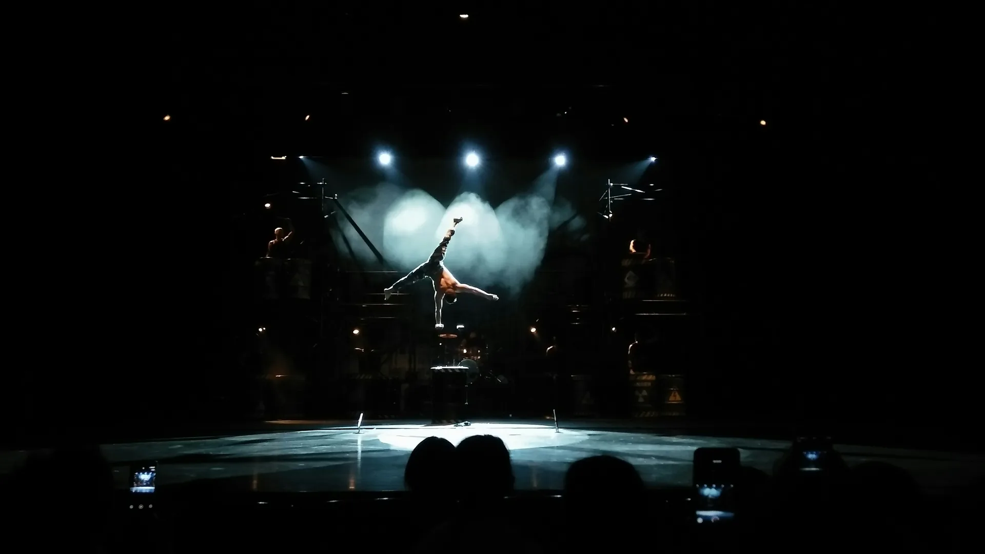 A Chinese acrobat balancing in a one-arm handstand under spotlights at a Shanghai acrobatics show
